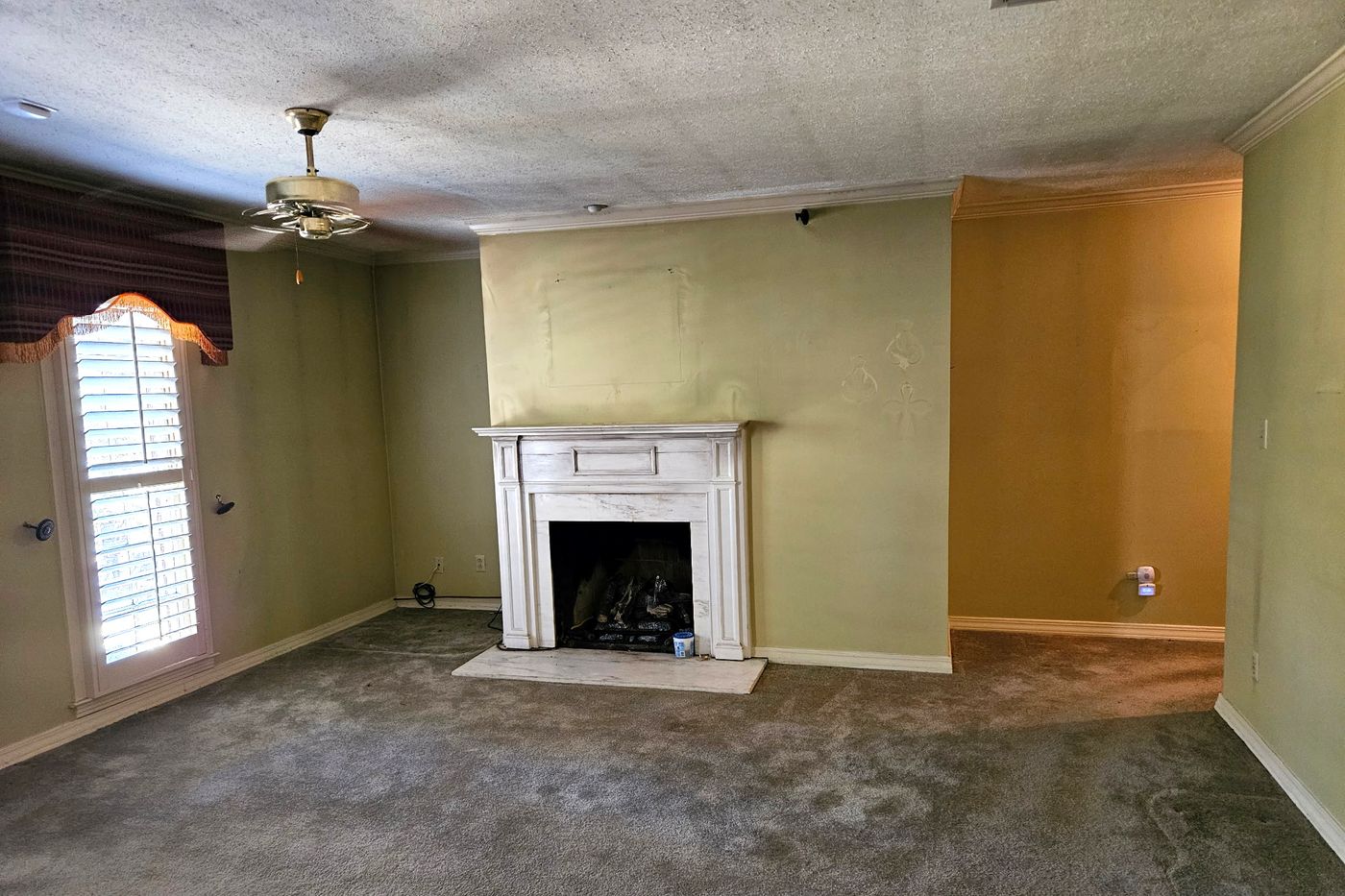 Primary bedroom with a white fireplace mantel on a raised hearth, a ceiling fan, and a shuttered window