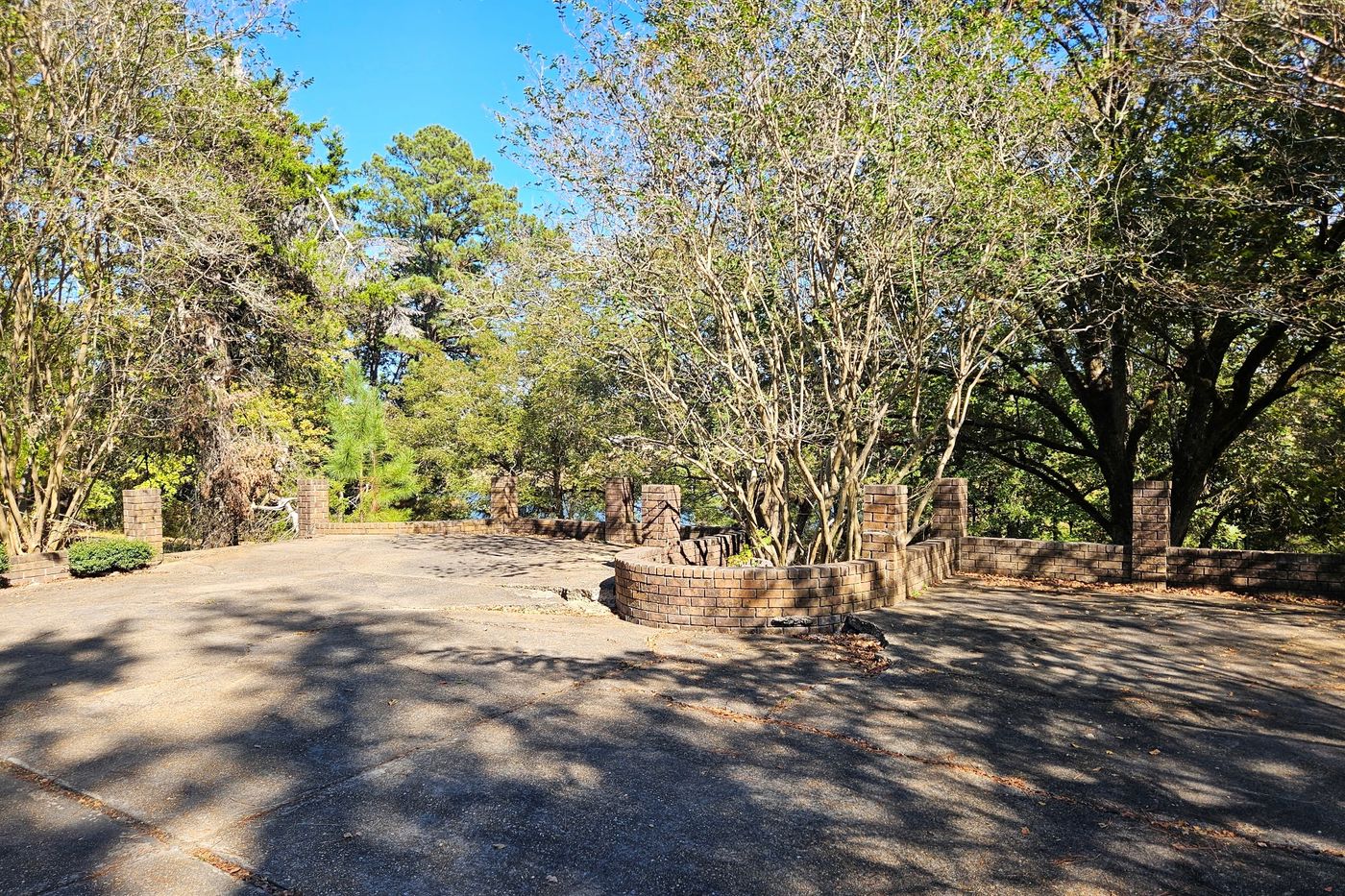 Paved circular drive edged by low brick walls and square brick piers, with a round raised brick planter of multi-trunk trees at the center